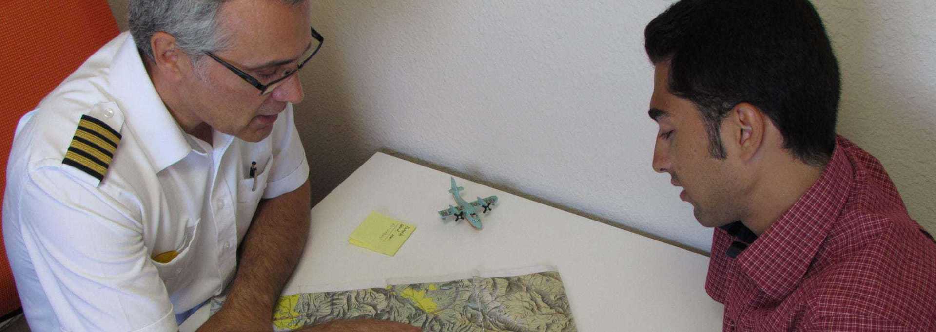 Older man and younger man examining a map at a table indoors.
