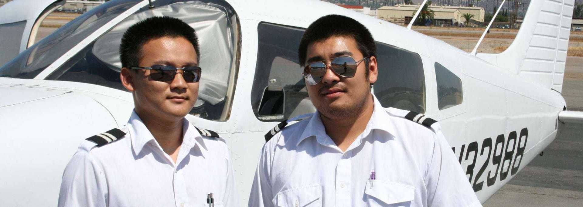 Two pilots in uniform standing beside a small aircraft on a sunny day.