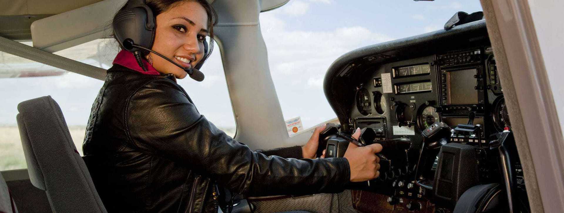 Person in cockpit operating airplane, smiling with headset on.